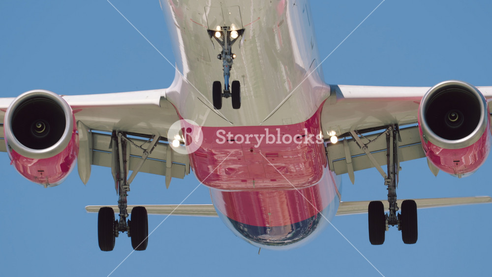 Front view passenger airplane flying overhead landing on runway in slow motion. Extreme close-up of colored aircraft with landing gear lands in airport. Warm sunny day, clear blue sky background