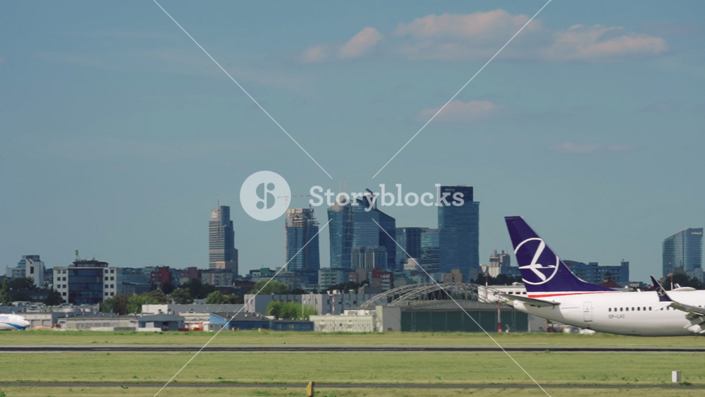 Warsaw, Poland - 03.07.2024: LOT airlines airplane landing on runway overlooking city downtown high-rise modern skyscrapers on horizon, slow motion. White aircraft lands on Chopin airport runway