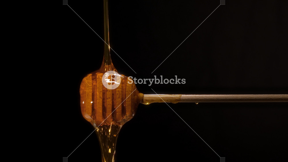 Close-up shot of wooden honey spoon, honey dipper stick and thick organic honey dripping, healthy food, tasty golden honey flowing, black background