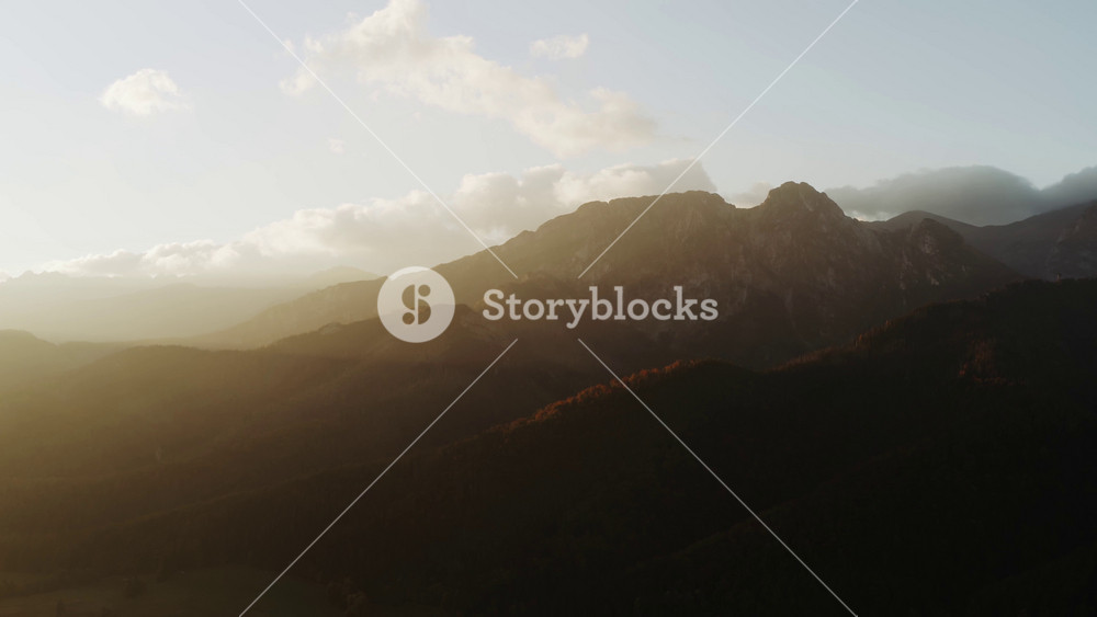 Aerial flight over amazing mountain range lit with soft golden morning sunlight. Drone shot epic mountain peaks in warm sunrise light. Picturesque highland landscape. Hiking inspiration concept