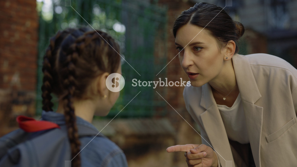 Close up view. Adult bullying the child on street. Young strict female teacher yalling at little girl while standing near school. Concept of