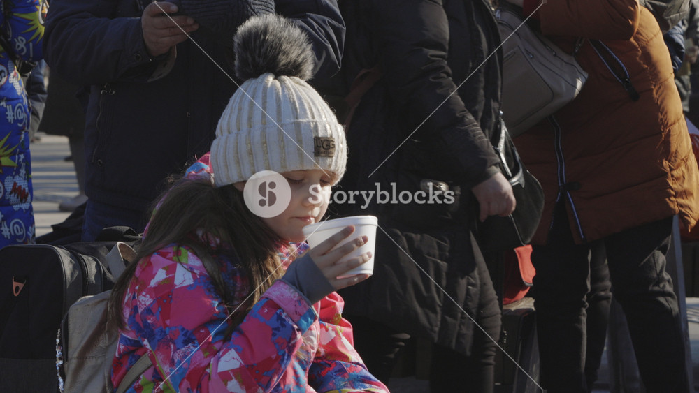 Lviv, Ukraine - March 15, 2022: Child sitting on the railway station and drinking at the street during the evacuation from Ukraine