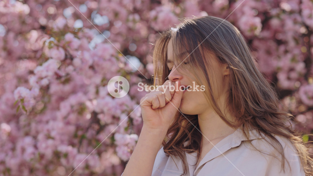 Caucasian young woman with natural brown hair coughing on street because of pollen allergy. Charming female looks sensitive to spring