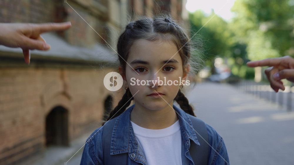 Close up of abusing little girl getting bullied outside near the school. Sad girl standing on the street and looking at camera. People