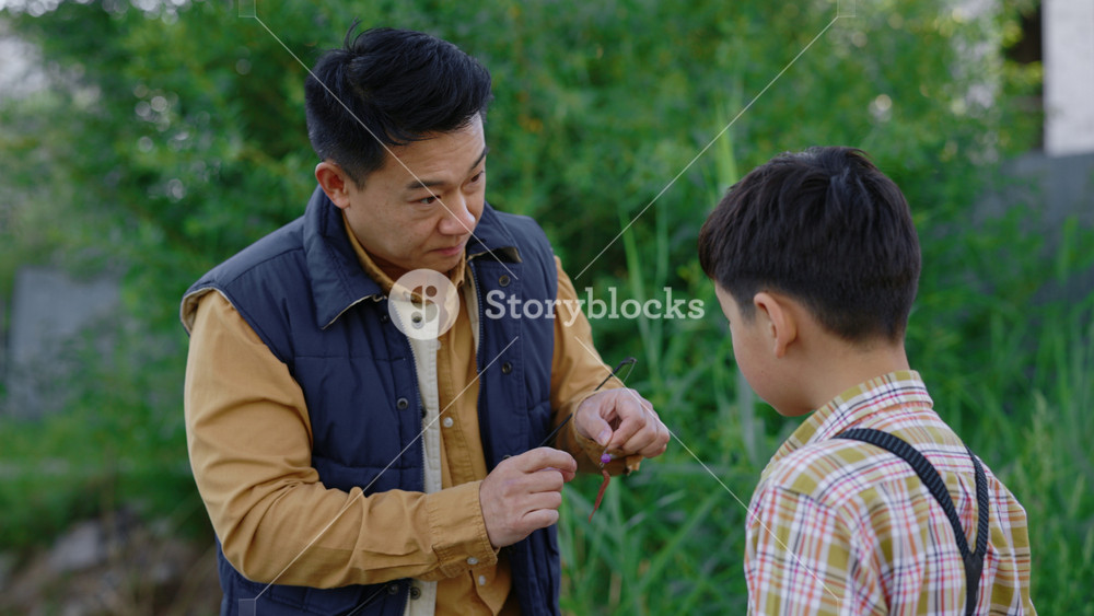 Close view of the asian father showing his son how to practice with fishing equipment before fishing. Dad shows child how to change the bait