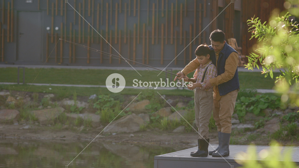 Asian father teaching his son how to cast a fishing into the local lake. Fishing. Family time together. Father-son relationships and fishing
