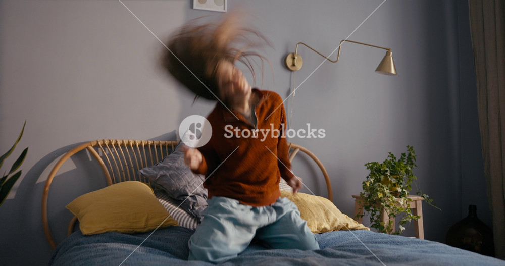 Zoom in girl in casual clothes spins her head with long hair and has fun at home during her dance to and improvisation to rock music in a