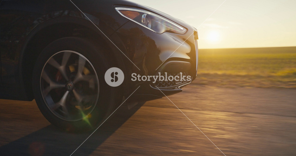 November 24 2024 Odesa Ukraine Close up a black Alfa Romeo Stelvio drives along a country road near green field with a yellow sunset in the