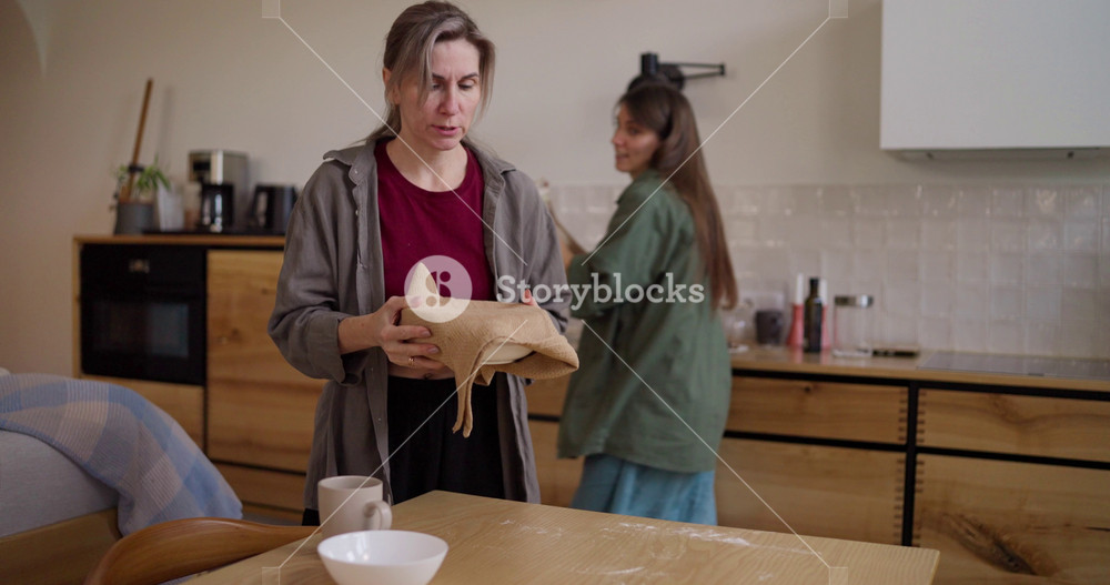 Focused blonde woman helping her brunette adult daughter prepare breakfast and working with her in the kitchen in the morning