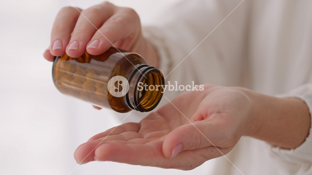 Woman hands pouring white pills from brown bottle close-up. Suggests healthcare, medicine, or supplements, highlighting daily wellness routines and personal health care. Vitamins for women's health