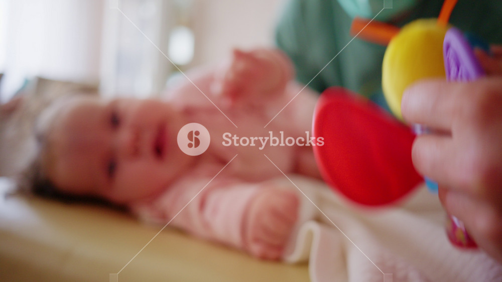 Healthcare professional wearing a medical mask gently supporting a baby during a pediatric care session with a colorful toy nearby