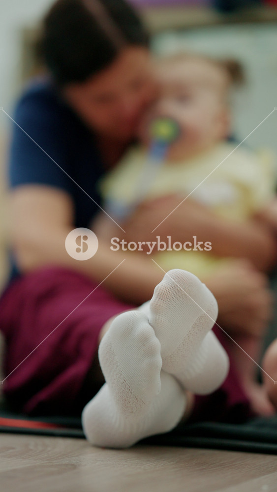 Close-up of baby's feet in white socks, an adult parent interacting with the child in a loving, nurturing moment