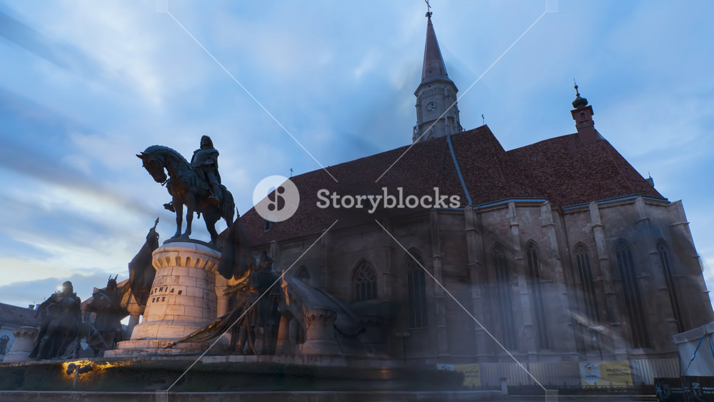 CLUJ, ROMANIA - APRIL, 2022: Timelapse view of Cluj centre at evening, Romania. Central square with Saint Michael Church and statue of Matthias Corvinus in front of it, walking people
