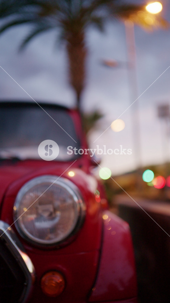 Cinematic close up of a red classic car headlight and curved hood with a blurred street background, capturing retro automotive style on the French Riviera