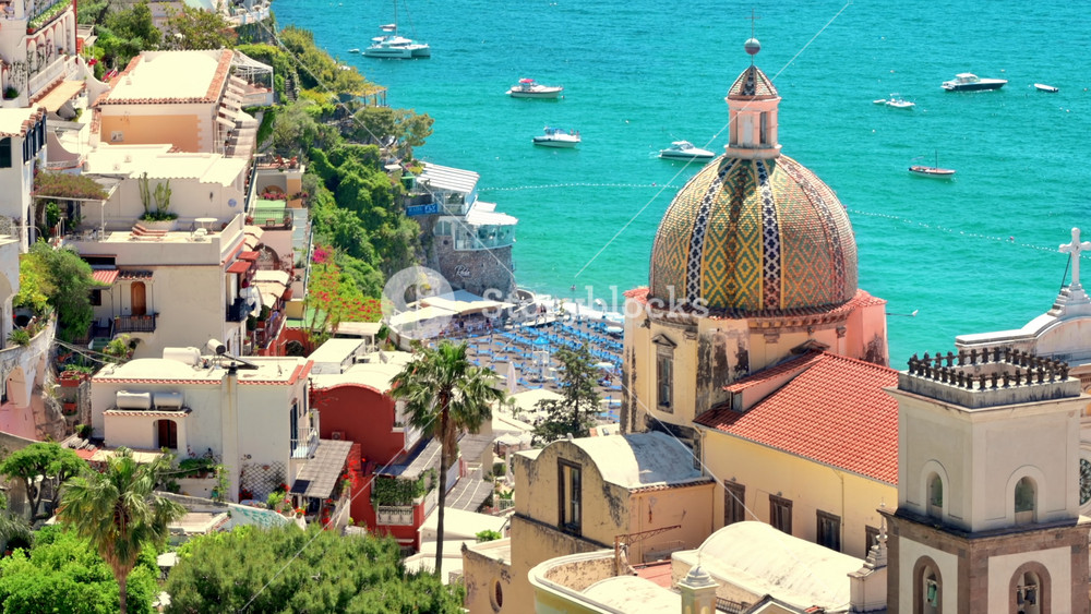 Street scape of Positano, located on the Tyrrhenian sea coast, Italy. Rows of residential buildings, church, greenery, beach with resting people