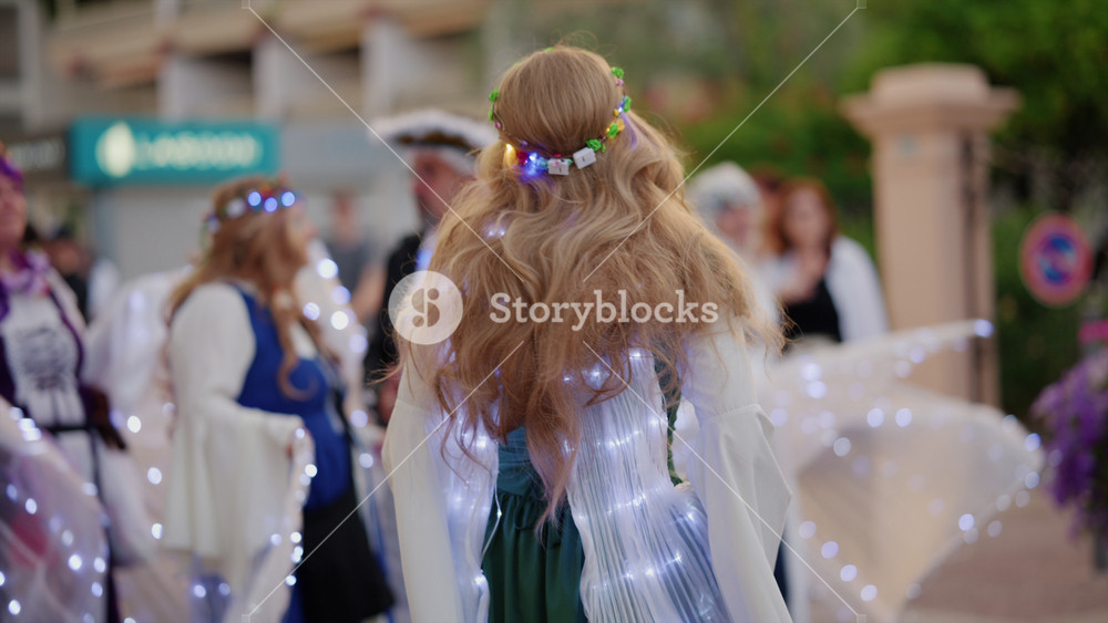 Antibes, France - June 25, 2026: Group of women in lit up fantasy costumes and floral headbands performing outdoors during a street festival celebration