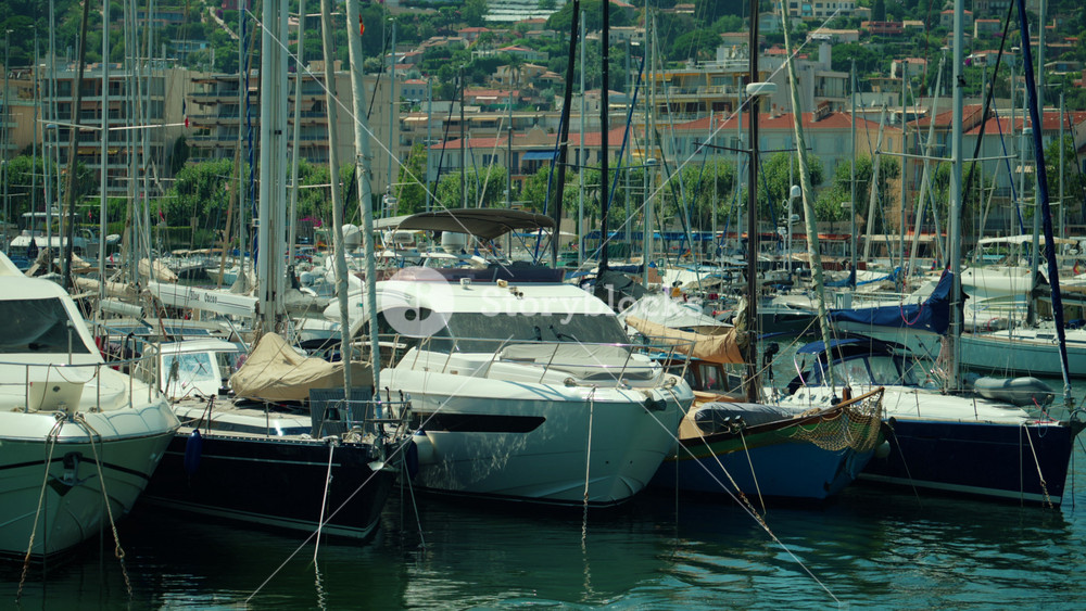 Boats docked closely together in a busy harbor, creating a scene of leisure and luxury against a hillside town backdrop, Antibes, France