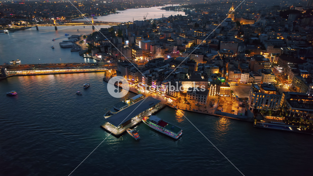 Aerial drone view of Istanbul at sunset, Turkey. Multiple residential buildings, mosques, Galata and Metro bridges over the Golden Horn waterway with multiple moored and floating ships, nightlights
