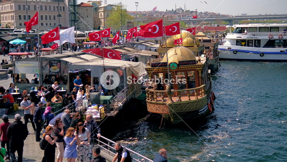 ISTANBUL, TURKEY - APRIL, 2022: Embankment street in the centre of the city. A lot of walking and resting people, moored boats, buildings