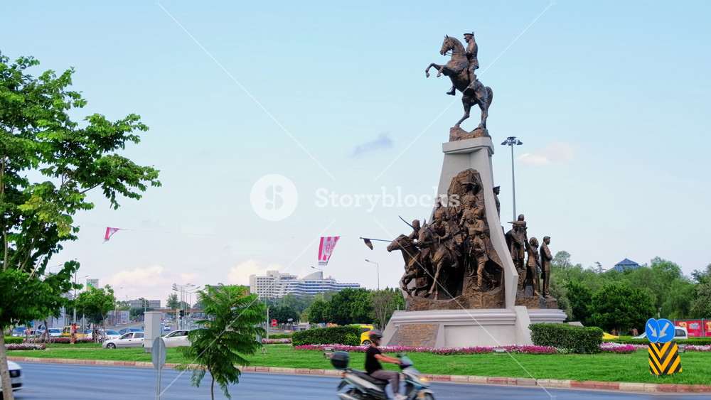 ANTALYA, TURKEY - SEPTEMBER, 2022: View of the monument to Mustafa Kemal Ataturk. Moving cars, greenery around it, cityscape on the background
