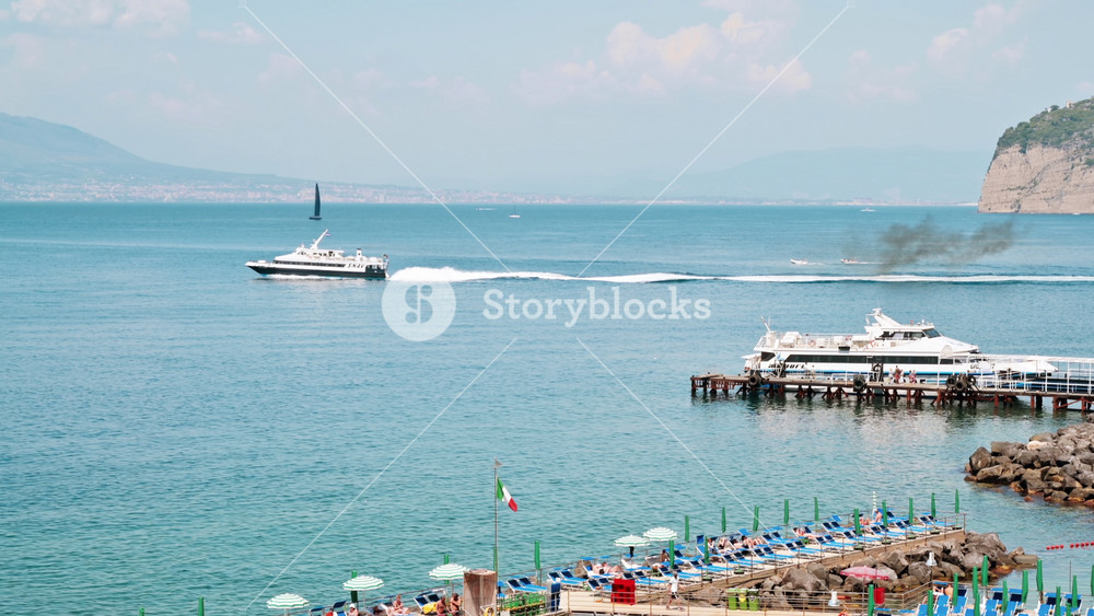 View of Tyrrhenian sea coast in Sorrento, Italy. Piers with sunbeds for resting, transparent water and seaport, floating yacht