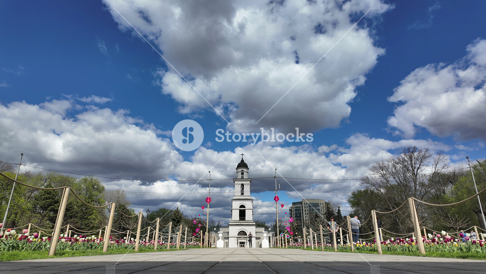 Chisinau, Moldova - March 28, 2024: Timelapse of Metropolitan Cathedral of Christ's Nativity surrounded by tulips with people walking by, and a cloudy blue sky