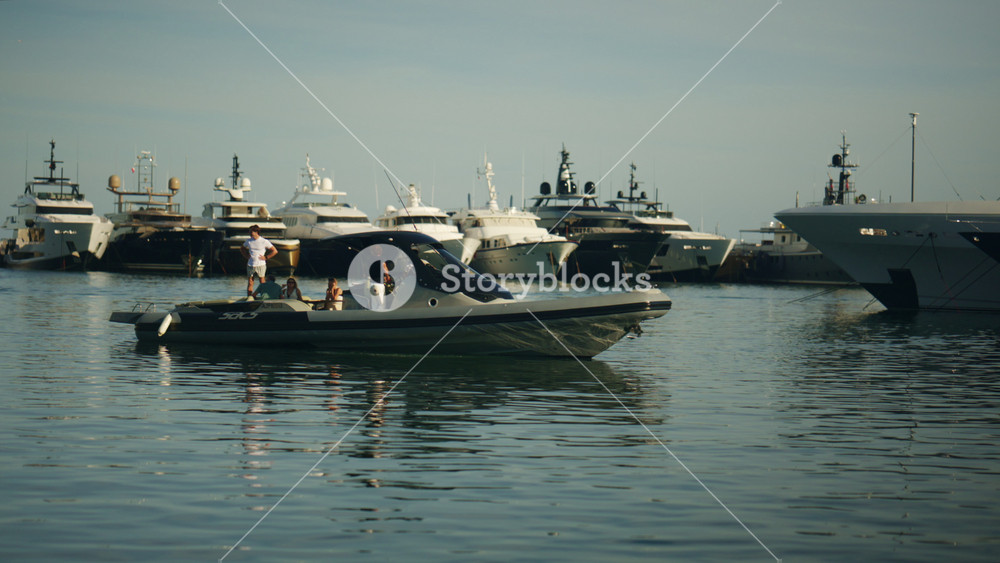 Antibes, France - June 8, 2026: Wide shot of a luxury marina with superyachts docked in calm water, a small motorboat passing by, and warm reflections on the sea