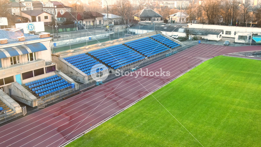 CHISINAU, MOLDOVA - JANUARY 15, 2021: Aerial drone view of Dinamo Stadium with tribunes, green grass, run paths, road on the background. Bare trees, winter