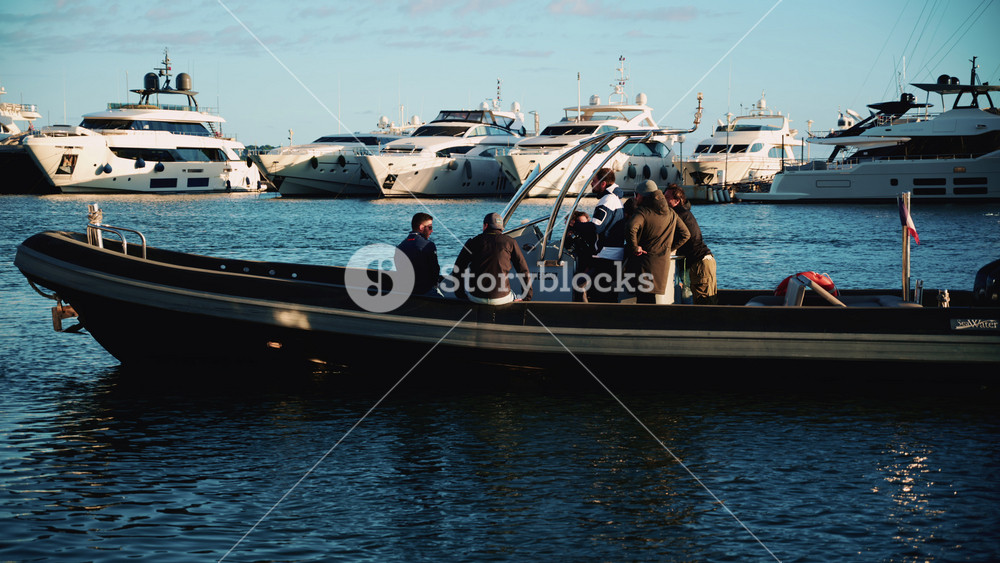 Cannes, France - December 23, 2025: Small group of people seated on a rigid inflatable boat near a harbor, with a large yacht anchored in the background