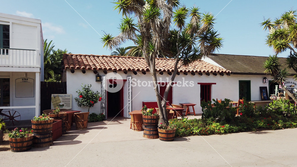 White house with clay roof, palm trees, and plants in front of the San Diego House Coffee and Tea shop in Old Town
