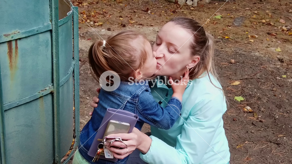 TEWKESBURY, MASSACHUSETTS - OCTOBER 7,2019: Young happy girl with blonde hairs kissing and embracing her mother in an autumn park. Slow motion
