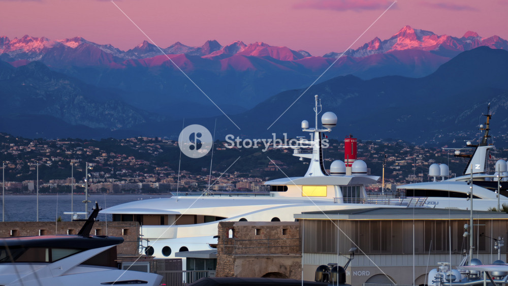 Juan-les-Pins, France - January 25, 2025: Multiple white boats docked in the harbour in Antibes with the mountains on the background at sunset