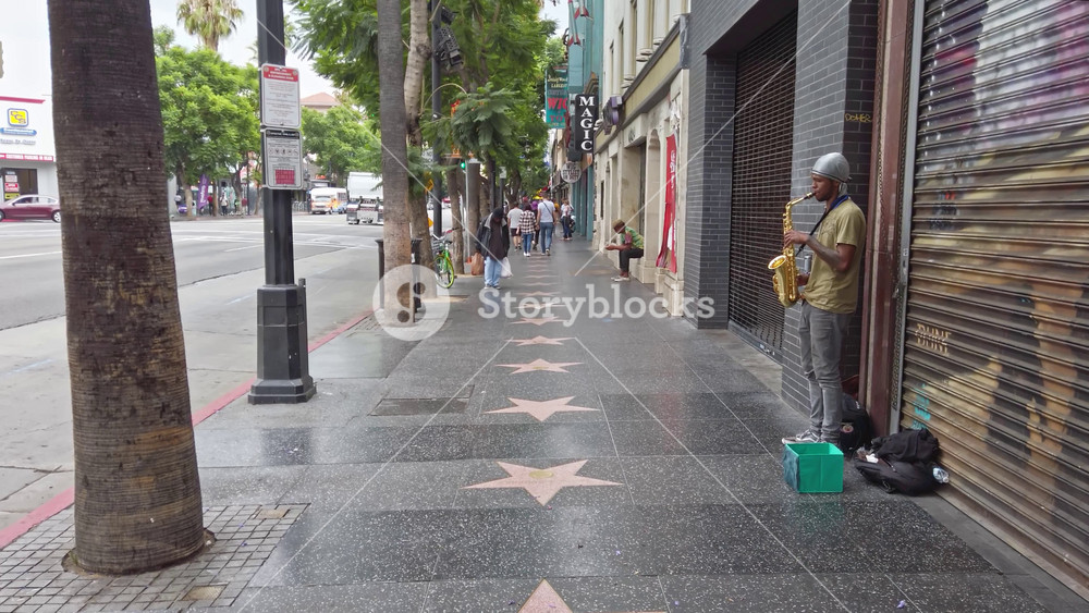 LOS ANGELES, CALIFORNIA - SEPTEMBER 26, 2019: Saxophonist sings on Hollywood Walk of Fame in daylight. People walking on the street. Bottom view