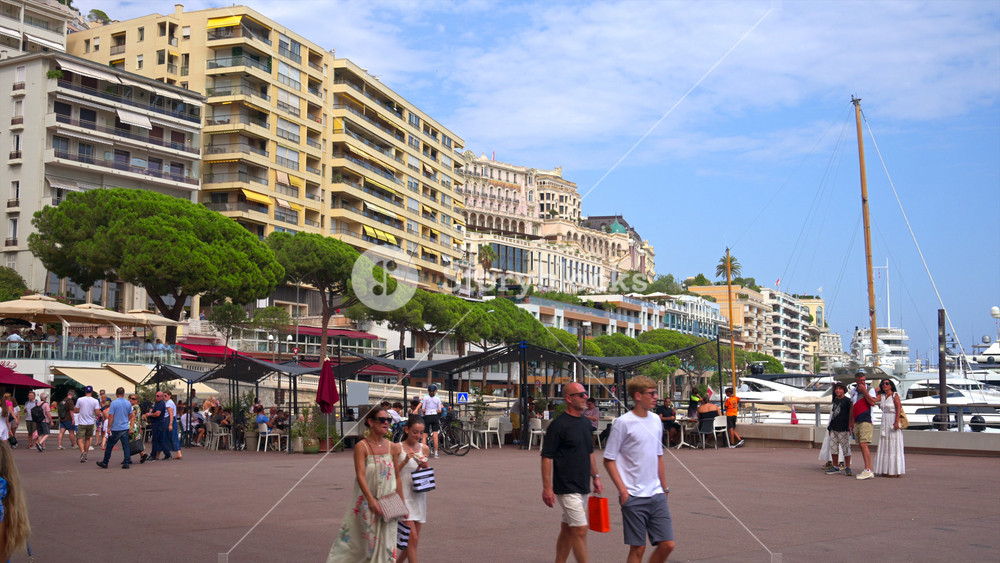 La Condamine, Monaco - August 25, 2024: People walking on a street near Port Hercules with the skyline of the city on the background