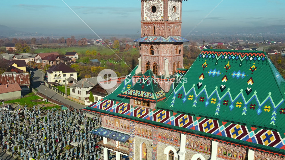 Aerial drone view of The Merry Cemetery in Sapanta, Romania. Church and multiple tombstones, visitors, residential buildings, yellowing trees