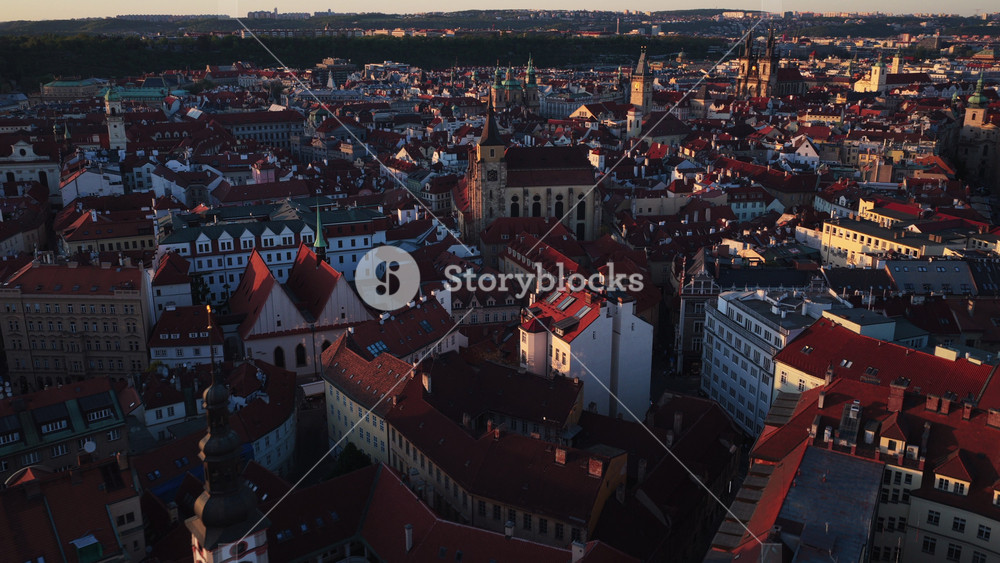 Aerial drone view of Prague old town at dusk with a wide spread of red-tiled rooftops, church spires, and Tyn Church silhouetted against a darkening sky, Prague, Czech Republic.