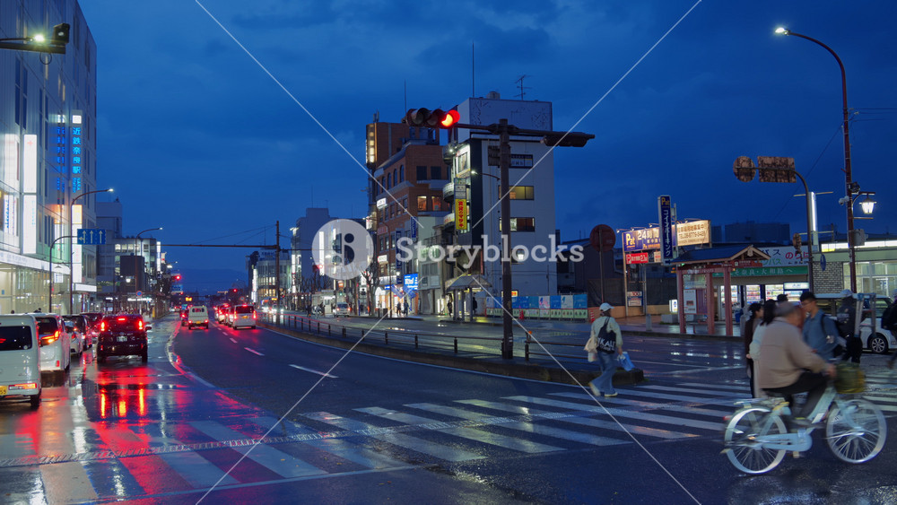 Nara, Japan - April 10, 2025: People crossing the street and cars moving through the city on a rainy evening. Translation: "Coin parking, Bus stop to Nara and Yamatoji"