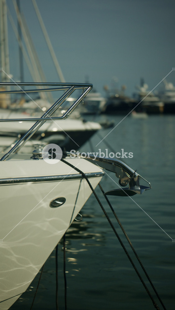 Close up of luxury yacht bows moored in a marina, showing ropes, railings, reflections on the water, and elegant nautical details
