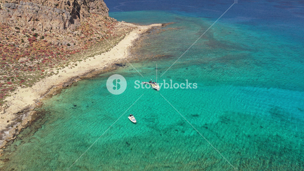 Aerial drone view of a sailboat anchored in crystal-clear turquoise water beside the sandy spit of Gramvousa island, Gramvousa, Greece
