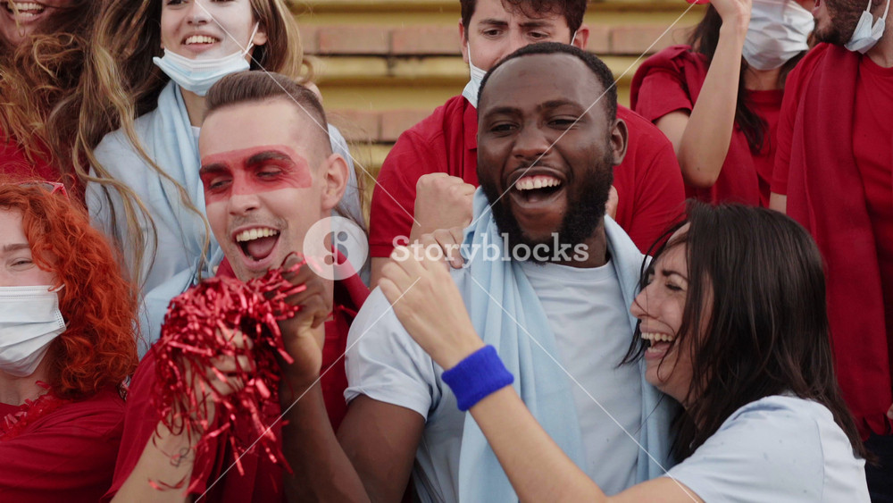Group of people of different races follow the soccer match in the stands. Men and women celebrating the victory dressed in their team's kit.
