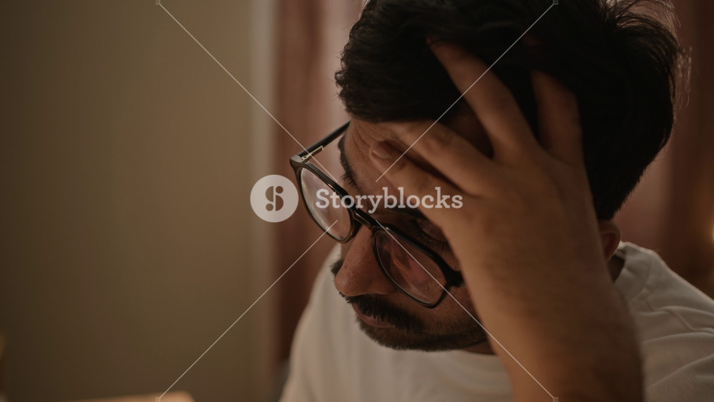 Closeup shot of Indian young man sitting at desk at home and rubbing eyes due to digital eye strain. Footage represents remote work burnout, mental fatigue, and wellness concepts