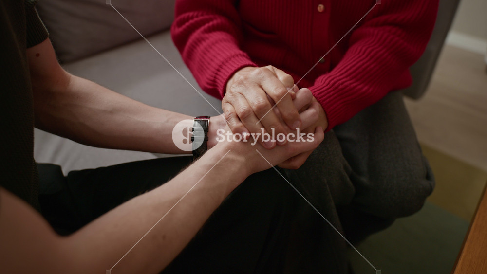 Senior Caucasian woman comforting young adult Caucasian man by holding hands and talking. Footage is ideal for senior care services, family support, and mental health awareness campaigns