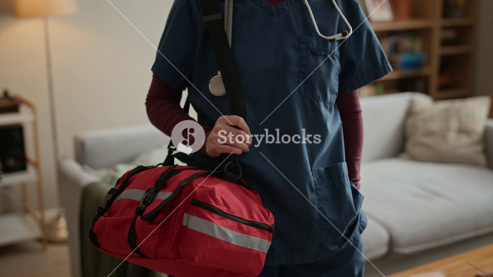 Portrait of middle aged Caucasian female nurse wearing scrubs and stethoscope, holding medical bag in living room. Footage is ideal for promoting home healthcare
