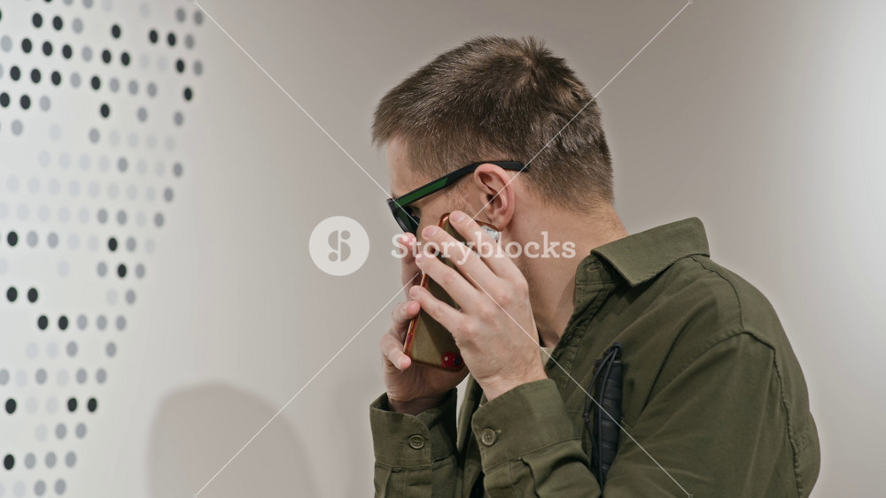 Close up shot of middle-aged Caucasian blind man wearing dark glasses using mobile phone to call his friend or listen to voice messages while standing indoors