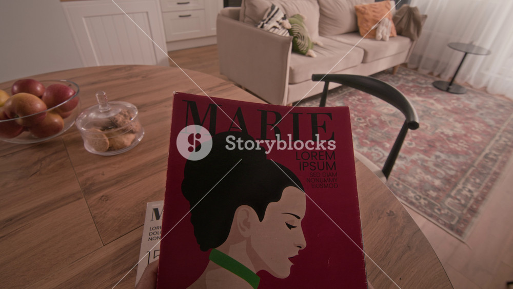 POV shot of young Biracial woman sitting down at table and starting conversation with her boyfriend sitting nearby and reading glossy magazines with colorful covers
