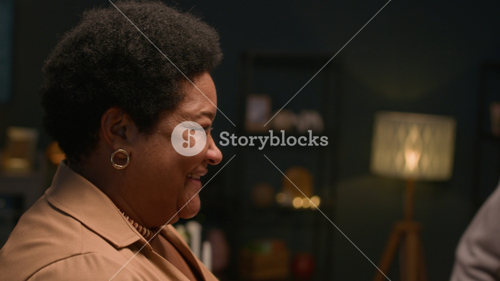 Close up on senior Black woman greeting adult daughter with gentle embrace then siblings hugging during festive evening dinner at home, happy family moment