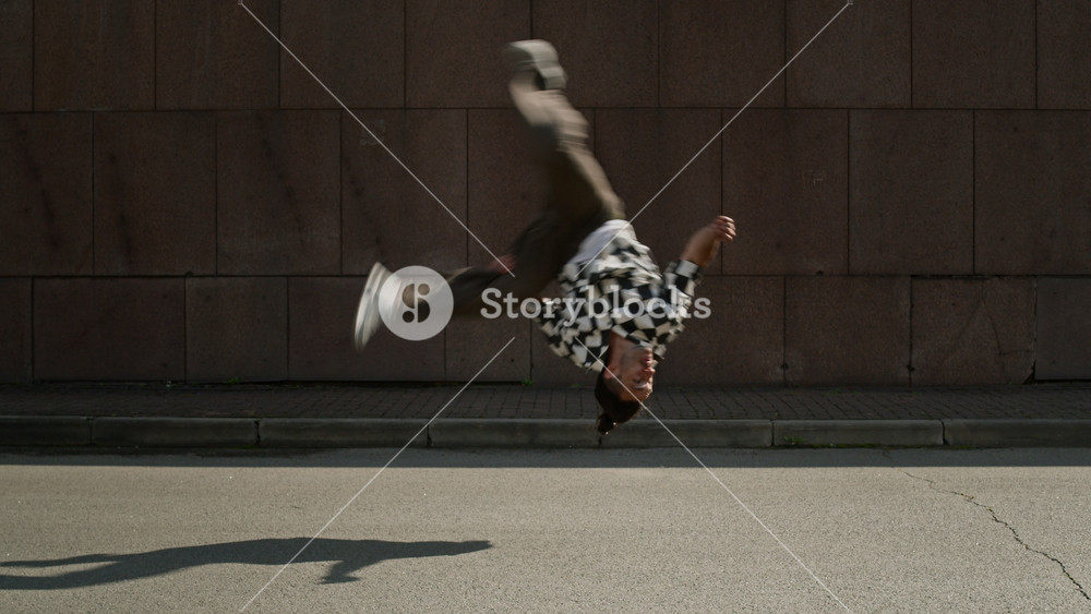 Full slowmo of acrobatic young Caucasian parkourist in urbanwear performing breathtaking side flip in front of concrete wall outdoors