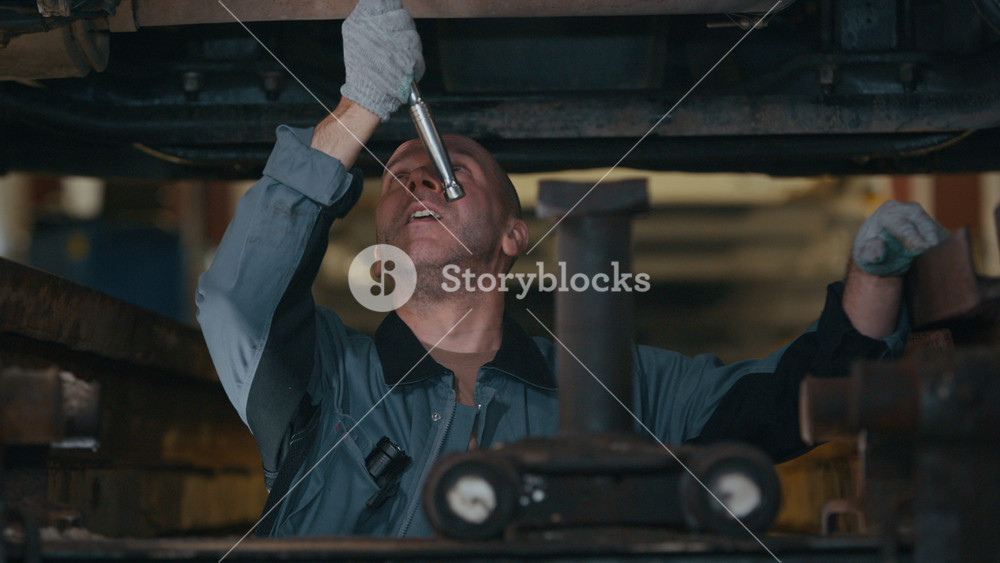 Medium shot of concentrated middle-aged Caucasian male mechanic in workwear and gloves repairing truck engine using car tool in auto repair shop