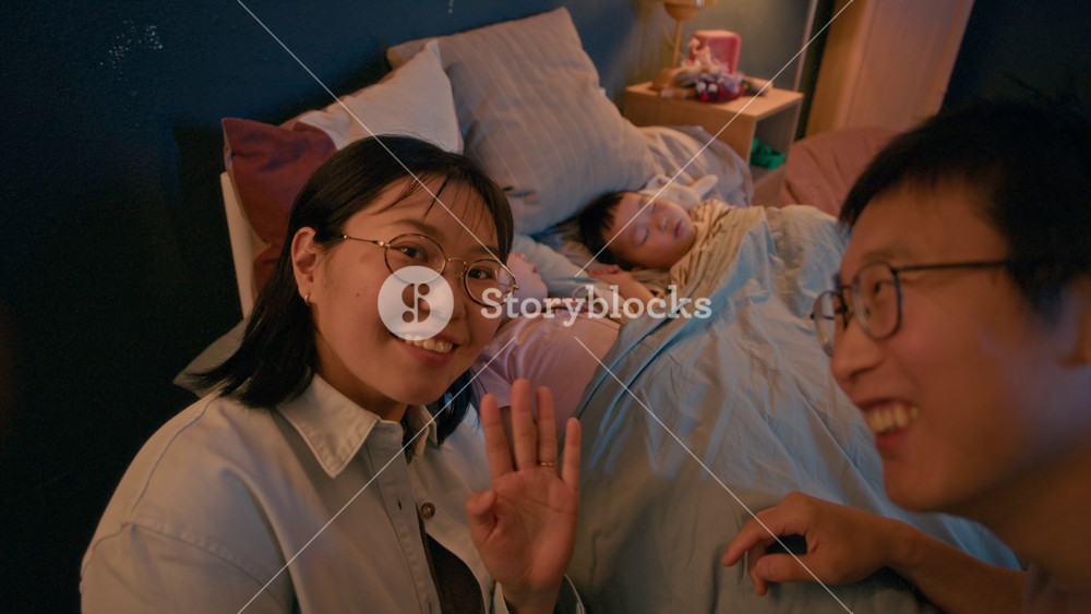 Handheld POV shot of young Asian parents filming homey family vlog while their two kids sleeping peacefully in their bed in cozy warm lit child bedroom