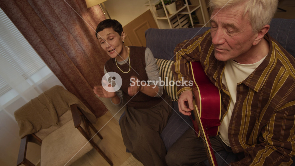 Slowmo shot of cheerful senior Caucasian woman singing along to guitar played by gray-haired happy man, spending nice evening together and sharing moment of joy